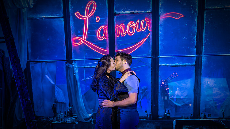 Hauptdarsteller küssen sich, im Hintergrund der Schriftzug „L´Amour“