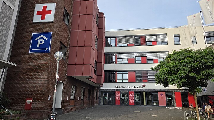 Außenansicht des St. Franziskus-Hospitals mit Haupteingang und rotem Kreuz
