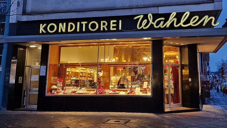 Außenansicht der Konditorei Wahlen am Abend mit beleuchteter Schaufensterauslage und goldenem Schriftzug