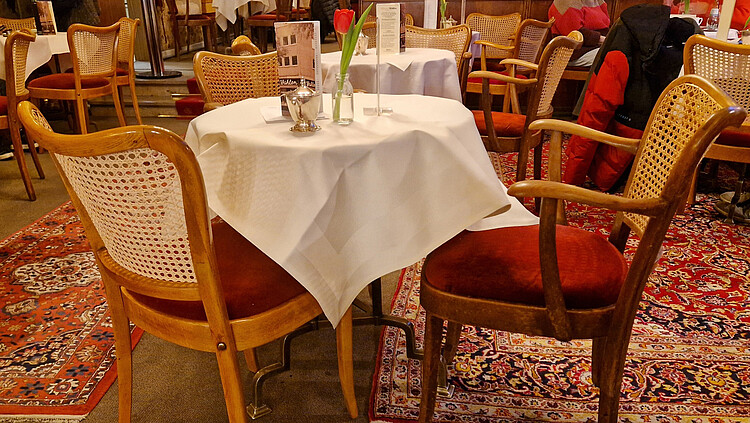 Weißgedeckte Tische mit Rattanstühlen mit rotem Samtpolster im Café Wahlen auf Perserteppichen